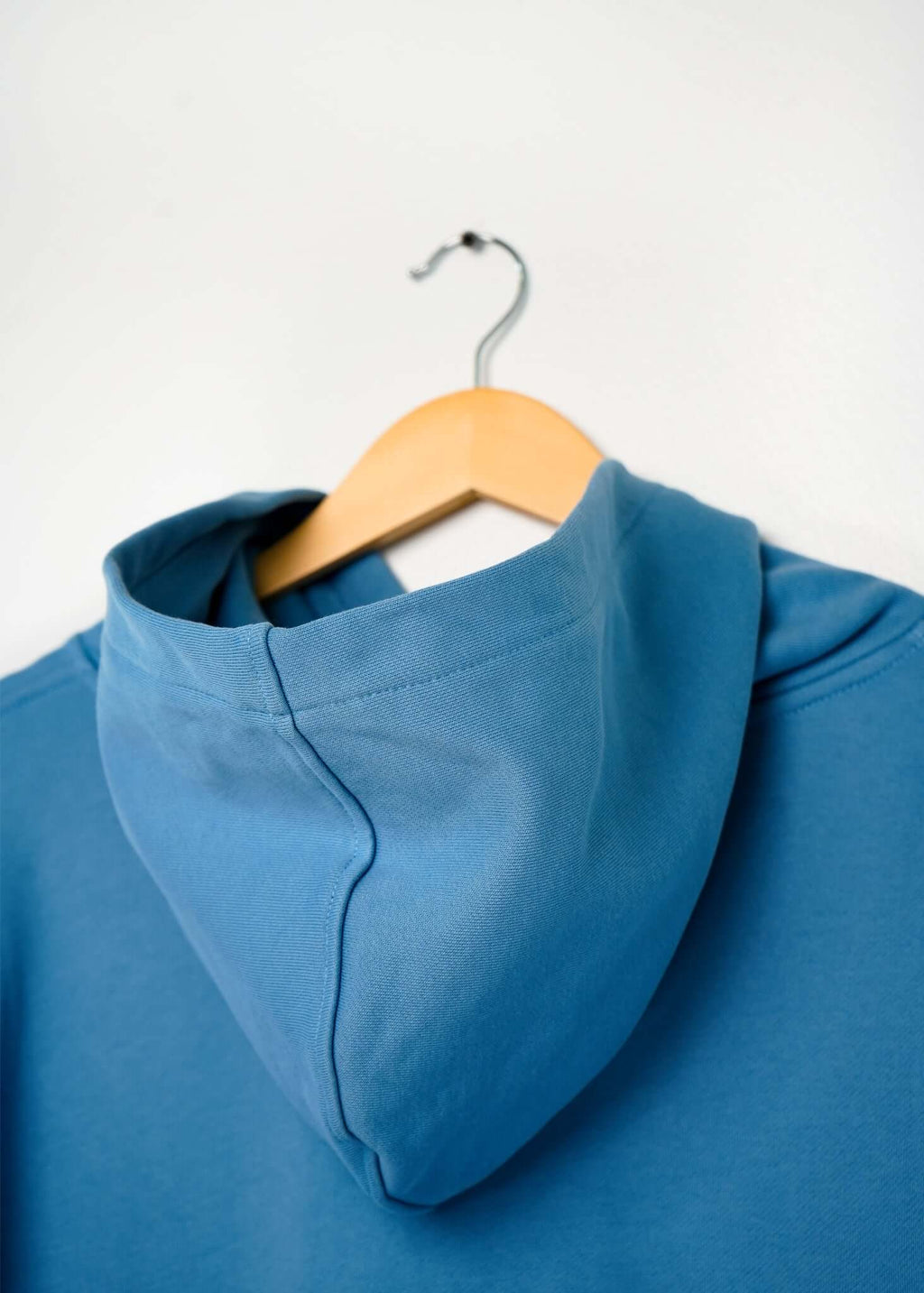 Back view of a lightweight terry hoodie hanging on a wooden hanger, showcasing the hood and soft fabric.