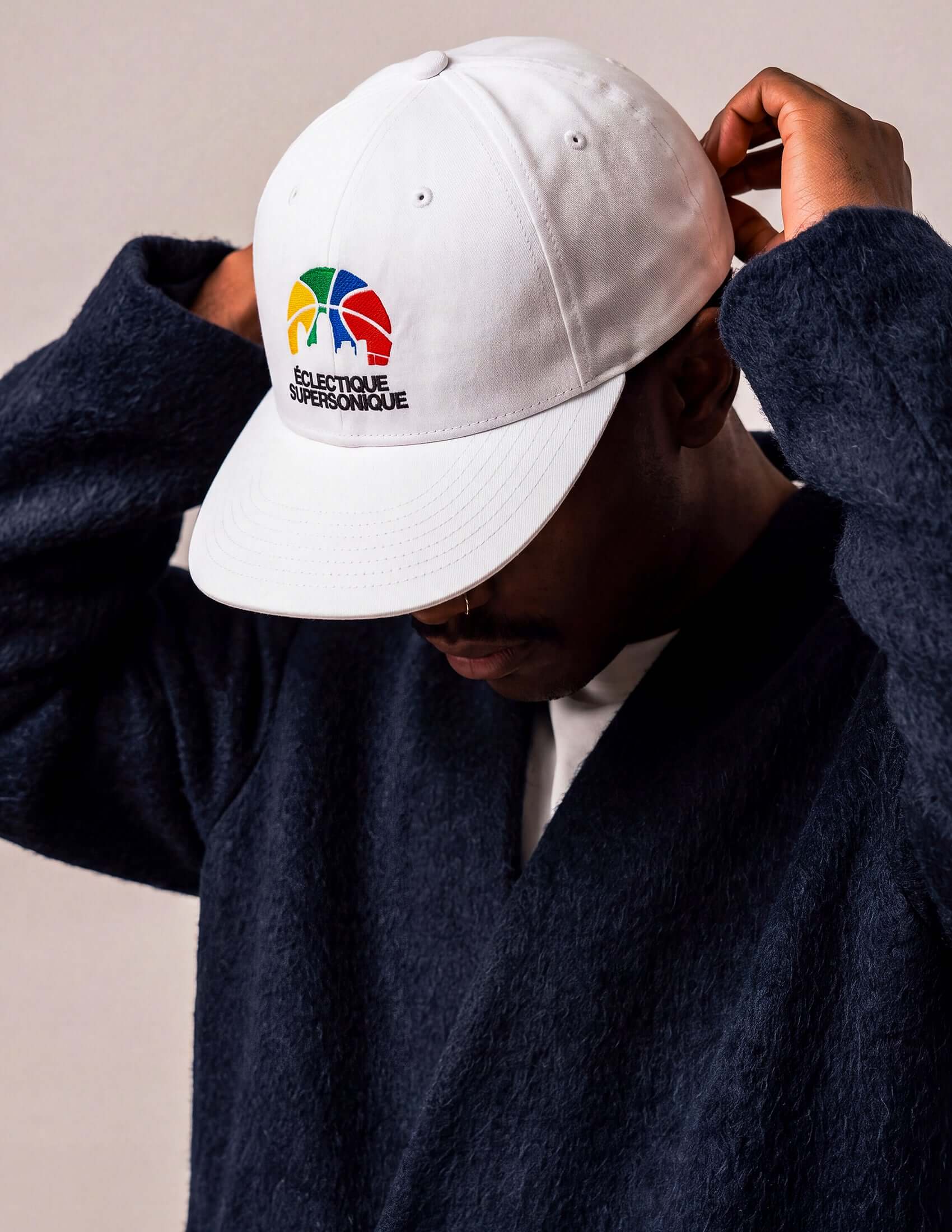 A person adjusting their Éclectique Super Sonique baseball cap featuring colorful embroidery.