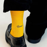 Close-up of yellow crew socks in Spectra worn with black shoes, showcasing their vibrant color and comfortable fit.